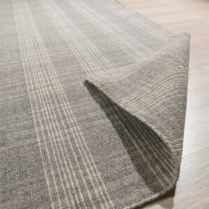 Heathered gray, striped rug with thin white lines rolled back on a shiny light wood floor.