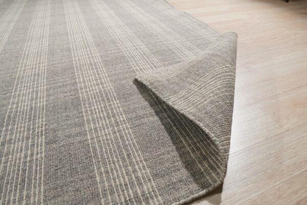 Heathered gray, striped rug with thin white lines rolled back on a shiny light wood floor.