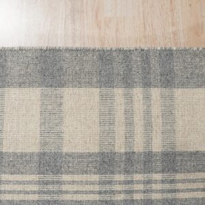 Gray and oatmeal striped rug corner with a flat texture lies on light blonde wood flooring.