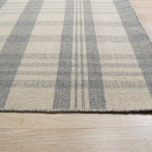 A flatweave rug with a gray and cream plaid pattern rests on light wood flooring.