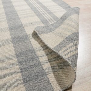 Low-pile grey and cream striped rug detail, showing woven texture and curled corner on a wood floor.