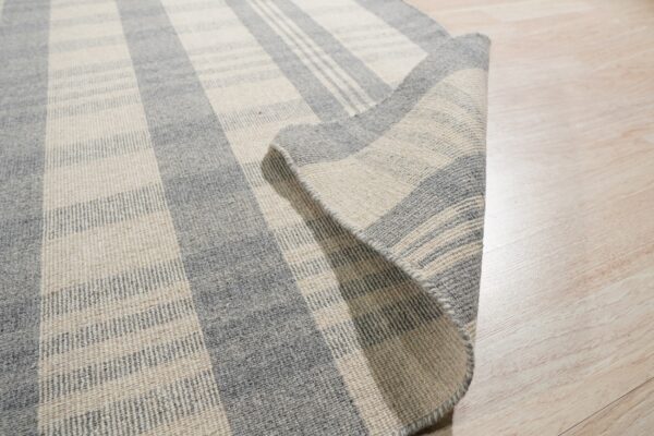 Low-pile grey and cream striped rug detail, showing woven texture and curled corner on a wood floor.