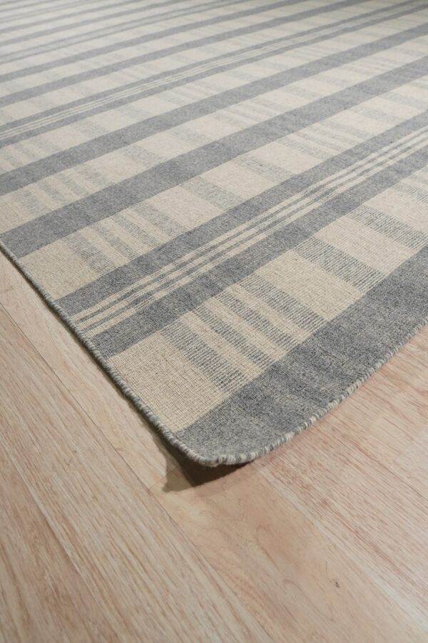 Gray and beige striped rug with a low profile texture resting on light wood plank flooring.