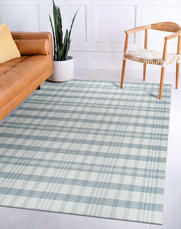 A low-pile blue and white plaid rug lies between a tan leather sofa and a light wood chair.