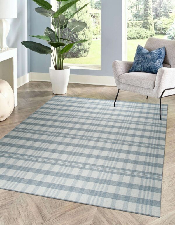 A low-pile blue and white plaid rug sits beneath a modern armchair on chevron wood flooring in a bright room.