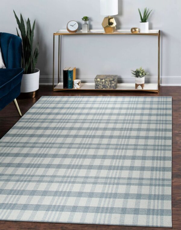 Light blue and beige plaid rug rests on dark wood flooring beside a blue chair and gold console table.