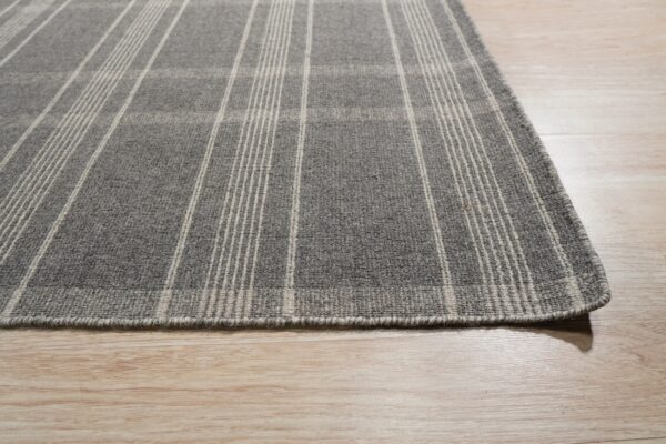 Low-pile heathered gray rug with cream plaid stripes rests on light wood planks.