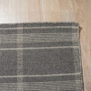 A corner view of a woven gray rug featuring a light beige plaid pattern on blonde flooring.