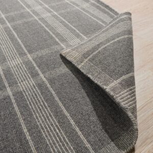 A dark gray plaid rug with light stripes is folded on a light wood floor.
