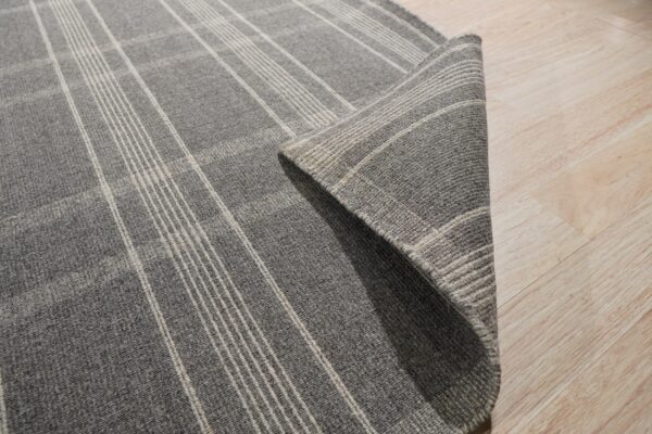 A dark gray plaid rug with light stripes is folded on a light wood floor.