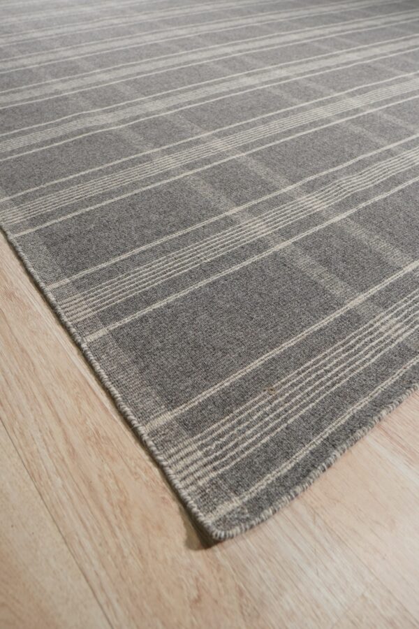 Gray low-pile rug with light plaid stripes angled across pale wood plank flooring.