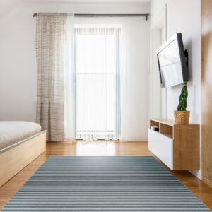 A blue and gray striped rug covers a wood floor in a brightly lit room with sheer curtains and light furniture.