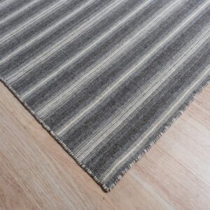 A corner of a low-pile gray and off-white striped rug rests on light blonde wood flooring.
