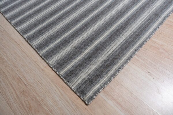A corner of a low-pile gray and off-white striped rug rests on light blonde wood flooring.