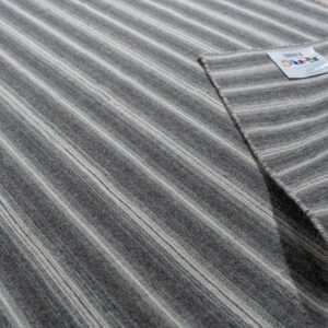 Close-up of a striped gray and cream rug folded on wood flooring, showing the low-pile texture.