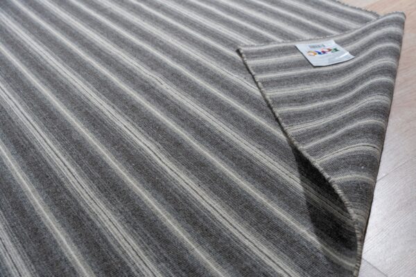 Close-up of a striped gray and cream rug folded on wood flooring, showing the low-pile texture.
