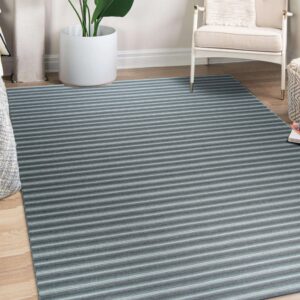 Gray and blue striped rug on wood floor next to a white armchair and potted plant.