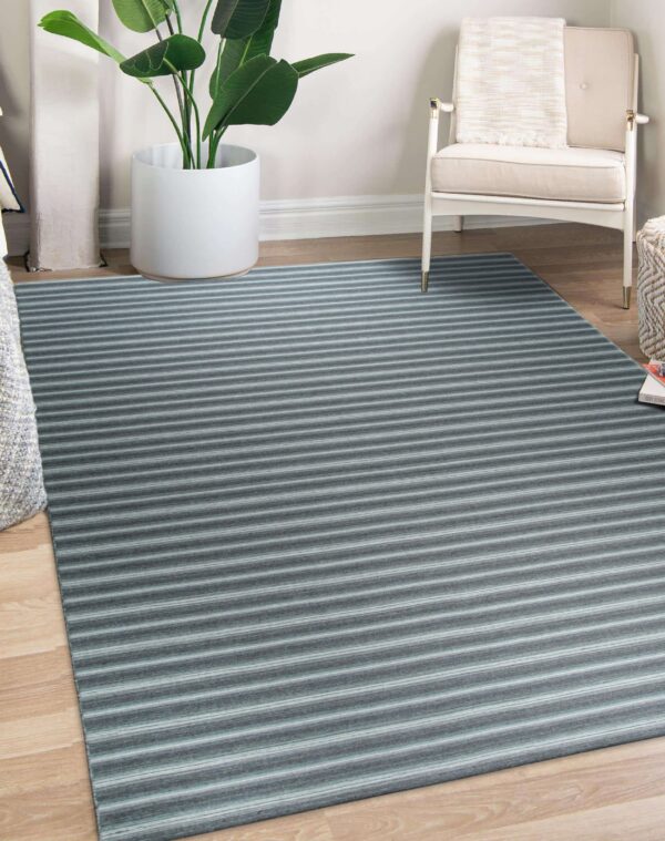 Gray and blue striped rug on wood floor next to a white armchair and potted plant.