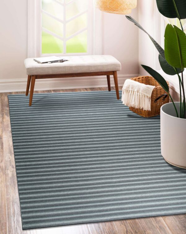 A narrow horizontally striped blue and gray rug covers hardwood floors beneath a bright window and upholstered bench.