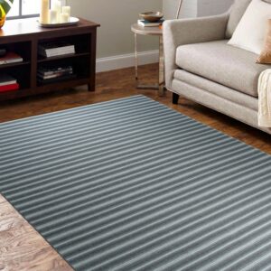 A gray and blue striped rug covers a wood floor beside a light beige armchair and dark cabinet.