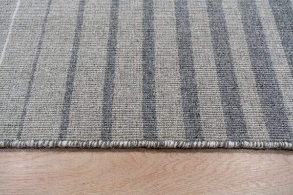 Light and dark gray striped rug with a textured low pile resting on blonde wood flooring.
