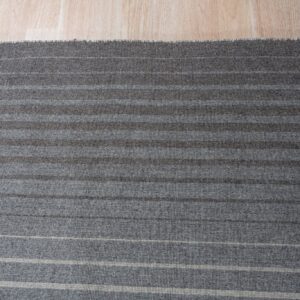 Gray striped rug with alternating light and dark bands sits on light wood plank flooring.