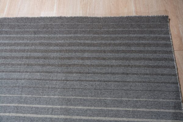 Gray striped rug with alternating light and dark bands sits on light wood plank flooring.