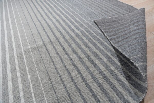 Light and dark gray striped rug on a wood floor, with the corner folded to show the reverse.