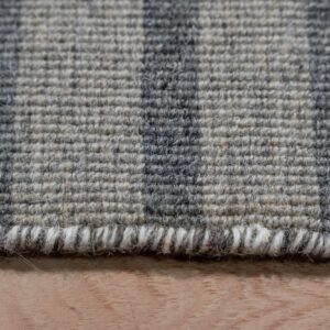 Low-pile gray rug with dark vertical stripes and a visible serged edge rests on light wood.