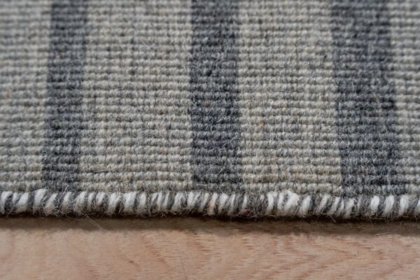Low-pile gray rug with dark vertical stripes and a visible serged edge rests on light wood.