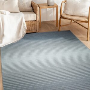 Low-pile rug with horizontal gray stripes transitions from light to dark blue on wood flooring near rattan chairs.