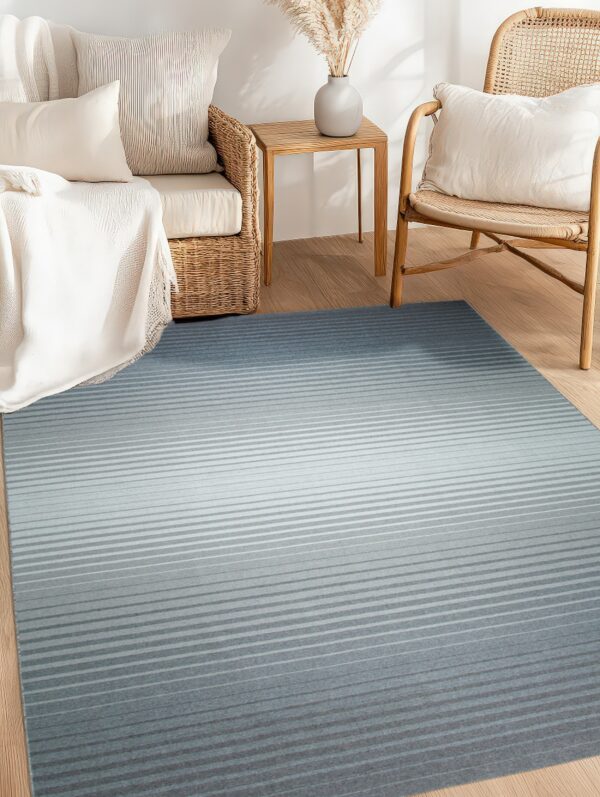 Low-pile rug with horizontal gray stripes transitions from light to dark blue on wood flooring near rattan chairs.