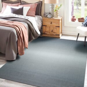 Teal and gray striped ombre rug covering light wood flooring next to a bed and nightstand.
