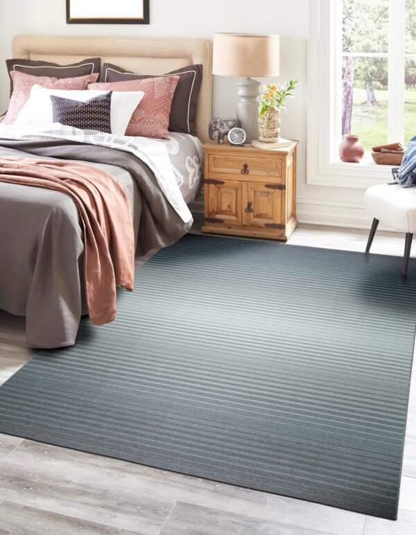 Teal and gray striped ombre rug covering light wood flooring next to a bed and nightstand.