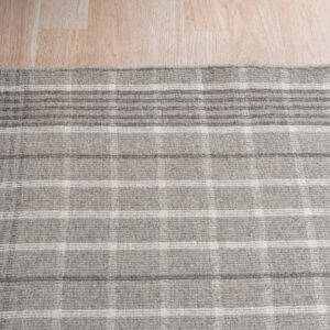 A gray and white low-pile rug with a plaid pattern rests on light wood plank flooring.