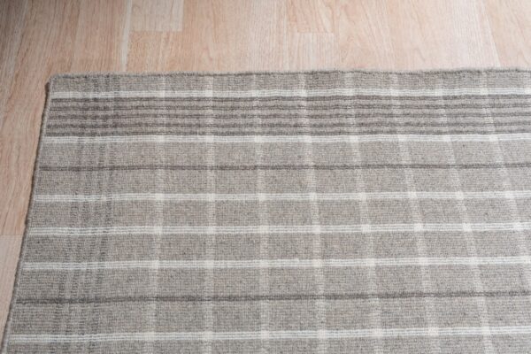 A gray and white low-pile rug with a plaid pattern rests on light wood plank flooring.
