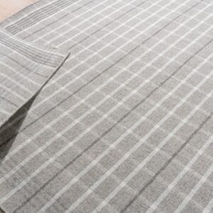 A gray flatwoven rug with a light plaid pattern is partially unrolled on light wood plank flooring.