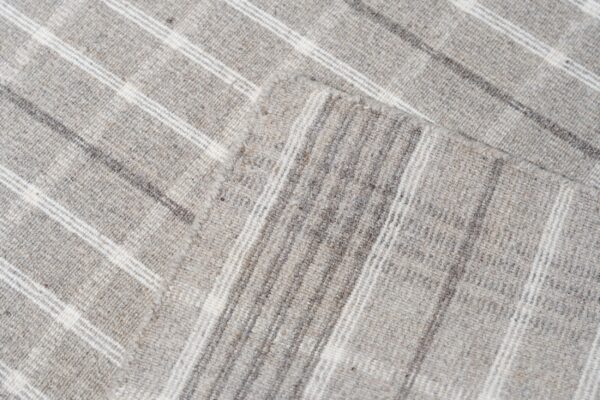 Low-pile heather gray rug folded, revealing a plaid pattern created by white and dark stripes.