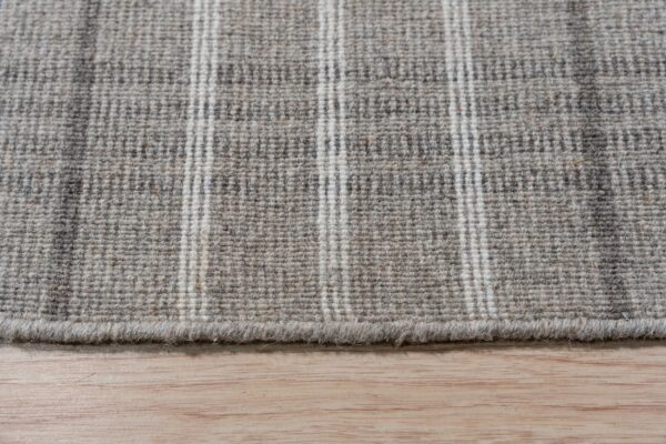A woven gray and cream striped rug texture rests on light wood flooring.