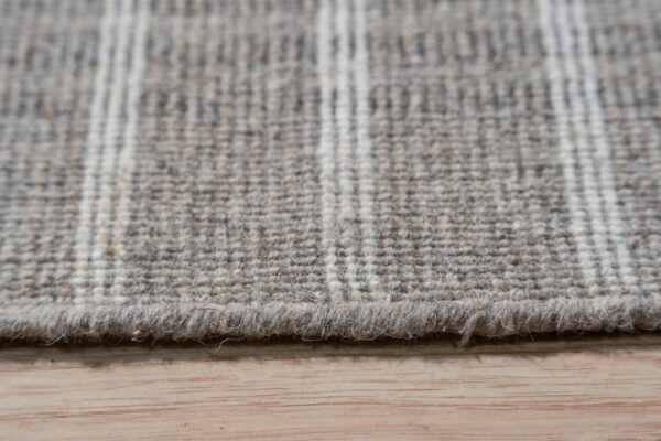 Textured, low-pile gray rug with subtle light stripes rests on a light brown wooden floor.