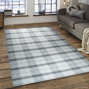 A large gray and white plaid rug covers distressed wood flooring beside a modern gray sofa.