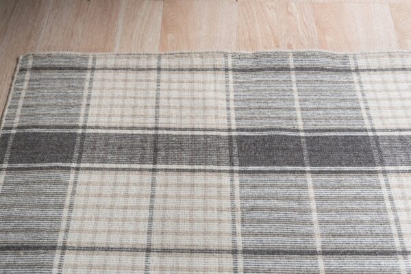 Textured gray and beige plaid rug lying on light wood plank flooring.