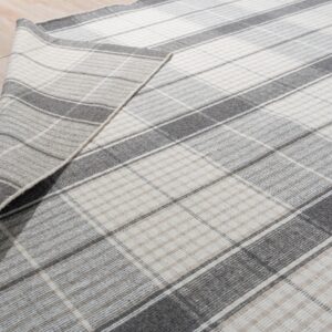 Low-pile gray and off-white plaid rug corner folded over light plank flooring.