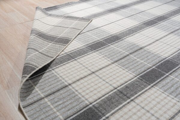 Low-pile gray and off-white plaid rug corner folded over light plank flooring.
