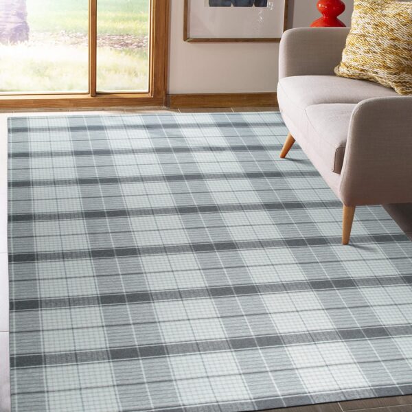 A gray and white plaid rug is placed on dark flooring partially covered by a light beige sofa.