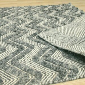 Textured gray and white rug featuring a chevron pattern, partially rolled back to show the woven backing on wood flooring.