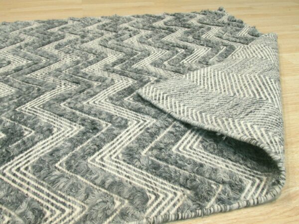 Textured gray and white rug featuring a chevron pattern, partially rolled back to show the woven backing on wood flooring.