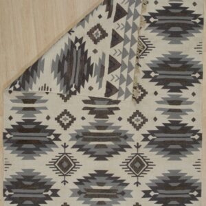 A cream flatweave rug with dark brown and gray Southwestern patterns rests on light wood flooring.