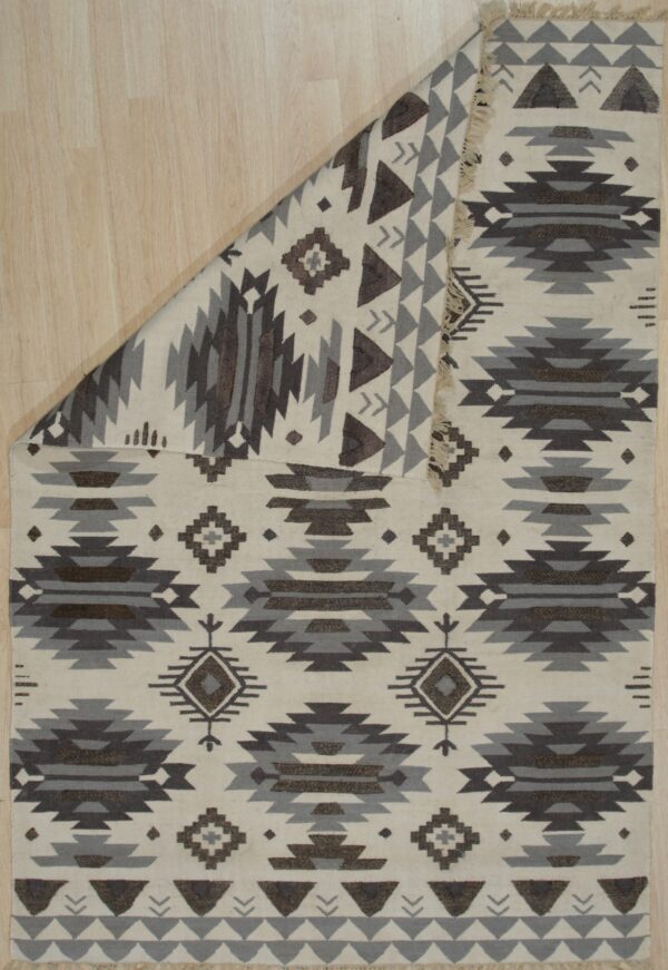 A cream flatweave rug with dark brown and gray southwestern patterns rests on light wood flooring.
