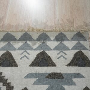 Low-pile rug with geometric patterns in cream, brown, and gray rests on pale wood planks.